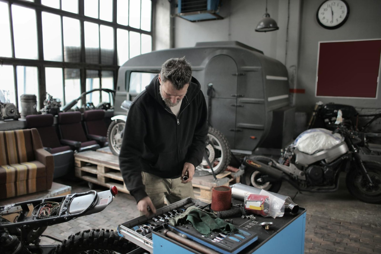 Bearded adult mechanic in casual clothes checking tools while working with vehicle in workshop